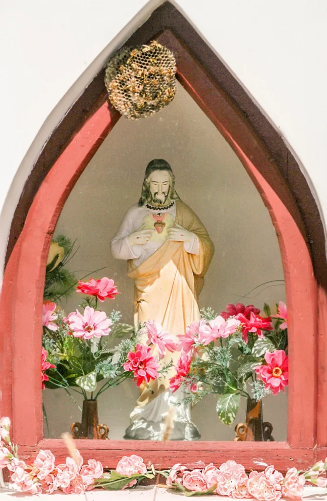 Kapliczka z figurą Jezusa wskazującego na Najświętsze Serce, ozdobiona kwiatami.