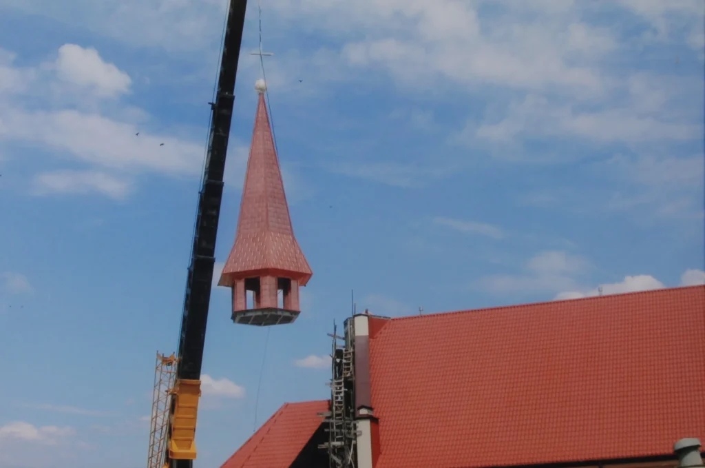 Montaż sygnaturki na dachu kościoła przy użyciu dźwigu