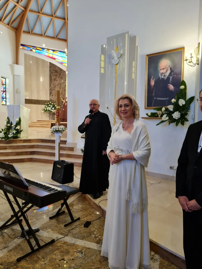 Renata Drozd w&nbsp;białej sukni i&nbsp;kapłan podczas uroczystości w&nbsp;kościele, obok instrumentu klawiszowego.